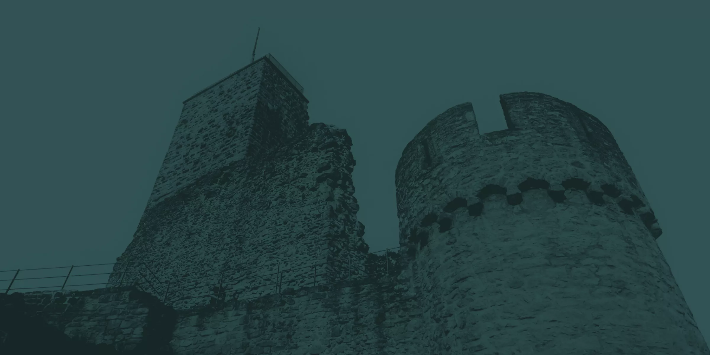 Schwarz-Weiß-Foto einer mittelalterlichen Steinburg mit zwei markanten Türmen, einem rechteckigen und einem runden, von unten gesehen, wobei die Beschaffenheit und das Alter der Steinmauern hervorgehoben werden.